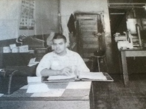 old black and white image of a man sitting at a desk with a binder open